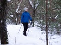 Winter activity. Adult caucasian woman in blue warm sportwear does nordic walking on the snow in the parkland outdoor Royalty Free Stock Photo