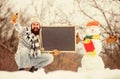Winter announcement. Hipster knitted hat and gloves show blackboard. Winter holidays. Guy and snowman snowy nature