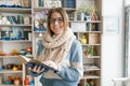 Winter autumn portrait of young beautiful girl student wearing glasses in knitted warm scarf and sweater reading book indoors Royalty Free Stock Photo