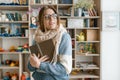 Winter autumn portrait of young beautiful girl student wearing glasses in knitted warm scarf and sweater reading book indoors Royalty Free Stock Photo