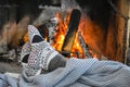 Young woman relaxing in front of cozy fireplace and warming up her feet in woolen socks in country house. Royalty Free Stock Photo