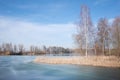 In winter, bare birches and other trees and bushes stand against a blue sky by a partially frozen lake in Bavaria Royalty Free Stock Photo