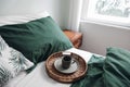 Winter breakfast in bed composition. Cup of coffee on wicker tray. Dark green linen bedding. Lifestyle composition