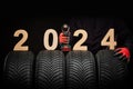 Winter car tires service and hands of mechanic with wheels screwdriver and text 2024 happy new year on black background Royalty Free Stock Photo