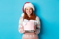 Winter and celebration concept. Adorable redhead girl giving you a present, wishing merry christmas, standing i santa Royalty Free Stock Photo