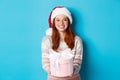 Winter and celebration concept. Beautiful redhead girl in santa hat wishing merry christmas, giving gift and smiling Royalty Free Stock Photo