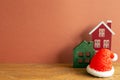 Winter christmas concept. Santa claus hat, house model on wooden table. red brown background Royalty Free Stock Photo