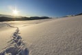 Winter Christmas landscape. Human footprint track path in crystal white deep snow through empty field, woody dark mountain range, Royalty Free Stock Photo