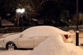 Winter in the city: a snow-covered car, snowdrifts, a burning lantern in the night city Royalty Free Stock Photo