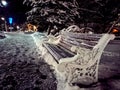 Winter city walks: snow-covered park bench with lanterns and trees on a winter evening