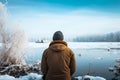 Winter clad man observes a frozen river from behind, serene moment