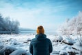 Winter clad man observes a frozen river from behind, serene moment
