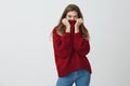Winter is close. Good-looking slender woman in trendy loose sweater hiding face in collar while glancing at camera