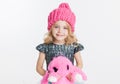 Winter clothes. Portrait of little curly girl in knitted pink winter hat isolated on white. Pink rabbit toy in her hands Royalty Free Stock Photo