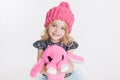 Winter clothes. Portrait of little curly girl in knitted pink winter hat on white. Pink rabbit toy in her hands Royalty Free Stock Photo