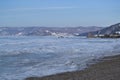 Winter coast iridescent with crystals white blue ice, the shore of lake Baikal l in snow, ships port mountains background