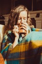 Winter cold sickness concept. Portrait Young freezing woman in comfortable chair with mug of tea wrapped in warm plaid blanket. Na