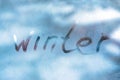 WINTER cold weather concept. Inscription word WINTER on the glass window with frozen patterns