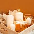 Winter composition. Burning candles and golden maple leaves on a beige background. Selective focus. Square photo.