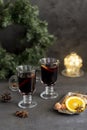Winter composition. Mulled wine in glasses at black background. Fir wreath, lights, tray with orange, cinnamon, nuts, cone and Royalty Free Stock Photo