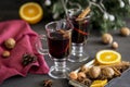 Mulled wine in glasses at black background. Fir wreath, tray with orange, cinnamon, nuts, cone and spices near