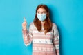 Winter, covid-19 and quarantine concept. Curious redhead girl in medical mask picking product, looking and pointing at