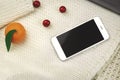 Winter cozy composition, tangerines, decoration and smartphone on blachround of kniteed warm sweaters, copy space