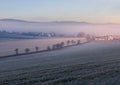 Winter czech landscape. Small village Lipi with trees in valley, agriculture field and misty fog at sunrise morning Royalty Free Stock Photo