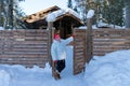 Elderly woman stands and smiles happily near the gate near a wooden house among the snowdrifts in the forest Royalty Free Stock Photo