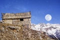 Winter evening landscape in french Alps. Old stone abandoned house on the mountain. Full moon on the sky, starry background Royalty Free Stock Photo