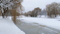 In winter everything is covered with snow, and the water channel in the city park is covered with thin ice and willow branches lea Royalty Free Stock Photo