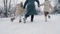 winter family activity outdoors. back view. Happy woman with 2 daughters are running on snowy road, in forest, during Royalty Free Stock Photo