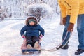 Little toddler child in winter clothes sitting in sledge ready to slide. His dad leaned to him. Dad and son have fun outdoors Royalty Free Stock Photo