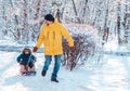 Winter family fun: father pulling sled with toddler child sitting in it. Dad and son have fun together Royalty Free Stock Photo