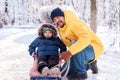 Winter family weekend: photo of toddler boy on walk with father in snowy day. Child sits in sled father sits kneeling, both laugh. Royalty Free Stock Photo