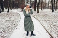 Winter fashion. Young woman wearing long green coat with scarf, hat, mittens and boots in snowy park Royalty Free Stock Photo