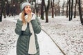 Winter fashion. Young woman wearing long green coat with scarf, hat, mittens in snowy park. Royalty Free Stock Photo