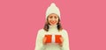 Winter festive portrait of happy smiling young woman holding red gift box in her hands wearing white knitted hat, sweater on pink Royalty Free Stock Photo