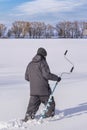 Winter fishing concept. Fisherman in action, going on snowy ice at lake with ice in hand