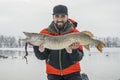 Winter fishing. Happy fisherman with pike fish at snowy lake Royalty Free Stock Photo