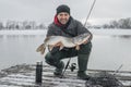 Winter fishing. Happy fisherman with pike fish at wooden platform Royalty Free Stock Photo