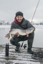 Winter fishing. Happy fisherman with pike fish at wooden platform Royalty Free Stock Photo