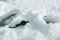 Winter fishing. Side view of small fishing rod lying on frozen water near hole drilled in ice, close-up