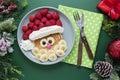 Winter food for kids. Christmas Santa pancake with raspberry and banana for children menu, green background, copy space