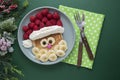 Winter food for kids. Christmas Santa pancake with raspberry and banana for children menu, green background, copy space