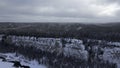 Winter forest landscape and pine tree forest growing on cliff over frozen river in snow. Clip. Breathtaking aerial view Royalty Free Stock Photo