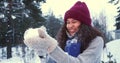 WINTER FUN. Beautiful young happy mixed race woman blowing on snow in warm mittens smiling at snowy forest slow motion. Royalty Free Stock Photo