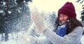 WINTER FUN. Beautiful young happy mixed race woman blowing on snow in warm mittens smiling at snowy forest slow motion. Royalty Free Stock Photo