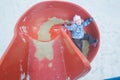 Winter fun of little girl on red plastic playground slide Royalty Free Stock Photo