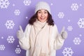 Winter girl with dark wavy hair wearing white warm sweater, scarf, cap and mittens standing with thumbs up isolated over studio Royalty Free Stock Photo